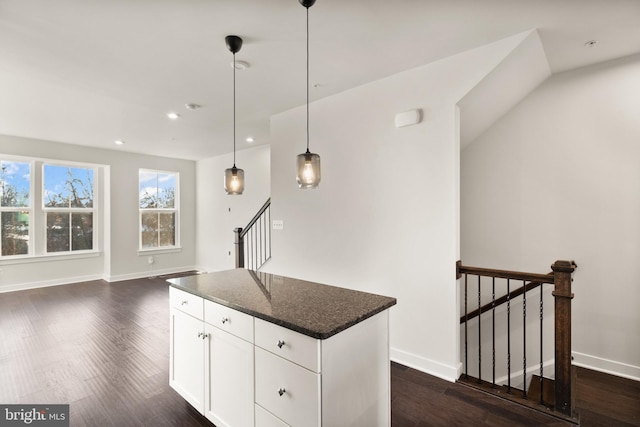 kitchen with dark hardwood / wood-style flooring, dark stone countertops, a kitchen island, pendant lighting, and white cabinets