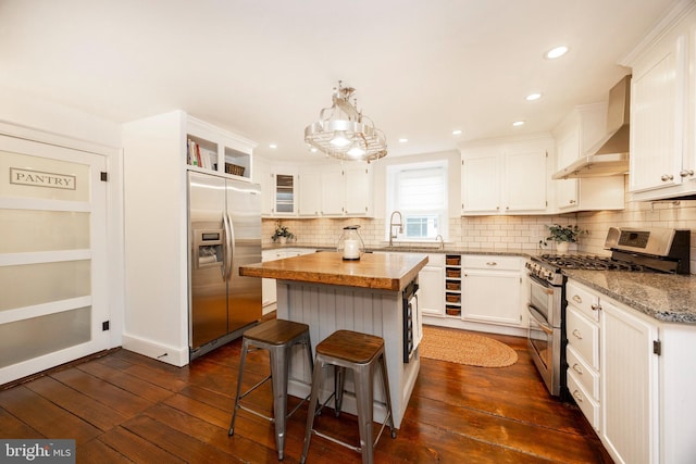 kitchen featuring stainless steel appliances, white cabinets, wall chimney range hood, a kitchen island, and light stone counters