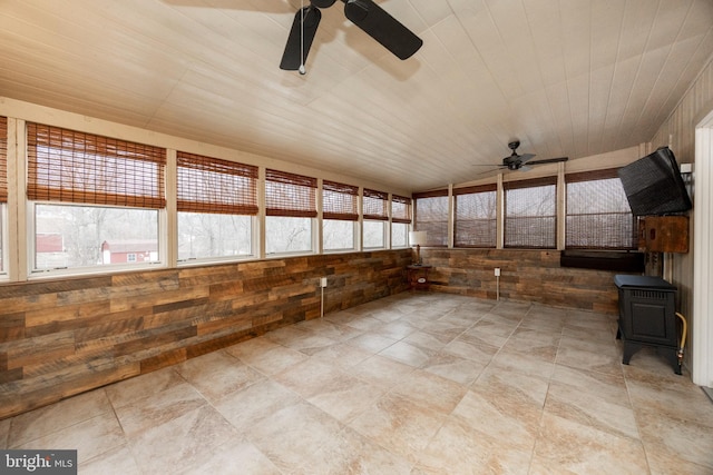 unfurnished sunroom with ceiling fan, a wood stove, and wood ceiling