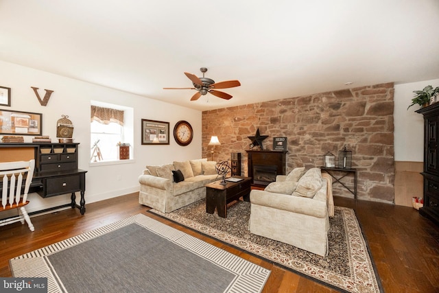 living room featuring ceiling fan, dark hardwood / wood-style flooring, and a stone fireplace