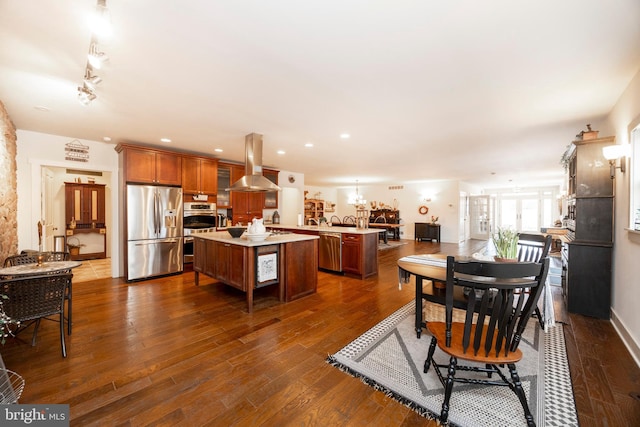 kitchen featuring dark hardwood / wood-style floors, a kitchen island, kitchen peninsula, island exhaust hood, and appliances with stainless steel finishes