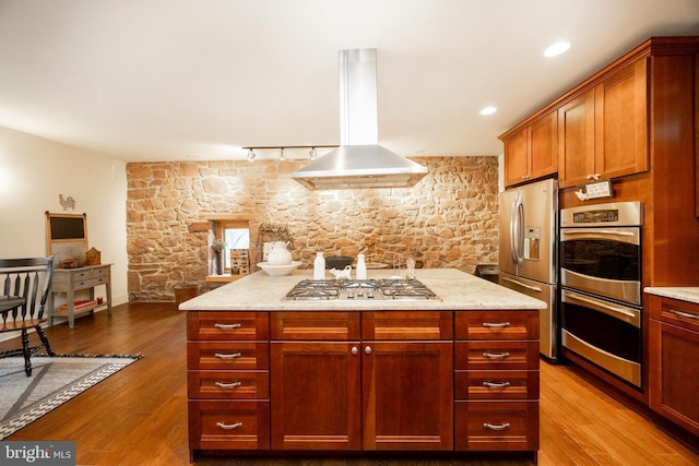 kitchen with island exhaust hood, light wood-type flooring, appliances with stainless steel finishes, light stone counters, and rail lighting