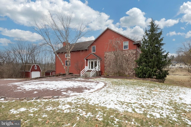 snow covered back of property featuring a garage and an outbuilding