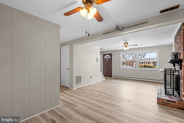 unfurnished living room with a brick fireplace, a baseboard heating unit, wood walls, and light hardwood / wood-style flooring