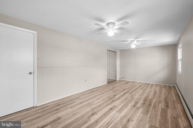 spare room featuring a baseboard heating unit, ceiling fan, and light hardwood / wood-style flooring