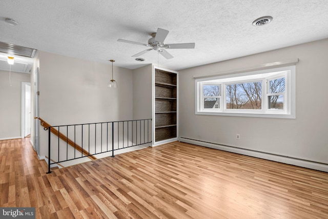 unfurnished room featuring a baseboard heating unit, built in features, a textured ceiling, and light wood-type flooring