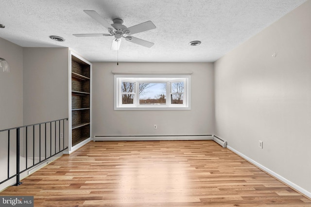 spare room featuring a baseboard heating unit, built in features, a textured ceiling, and light hardwood / wood-style flooring