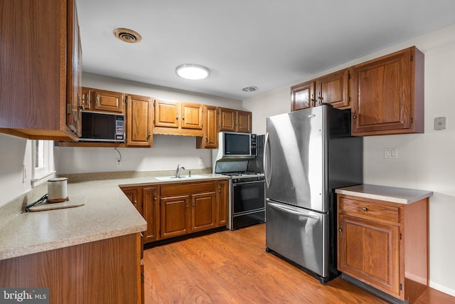 kitchen with gas stove, sink, stainless steel fridge, and light hardwood / wood-style flooring