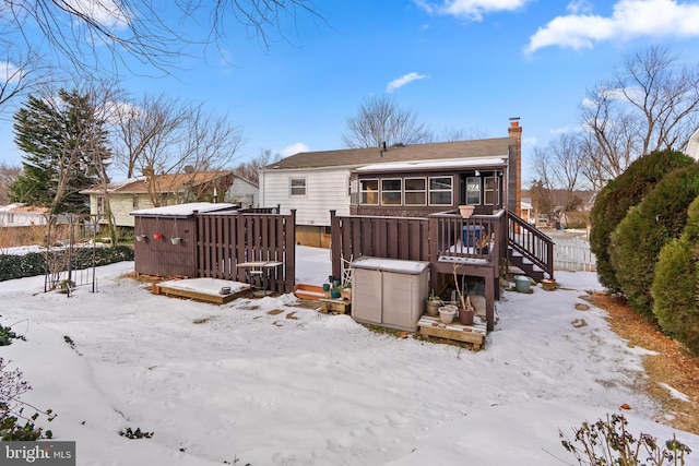 snow covered house featuring a wooden deck and a sunroom