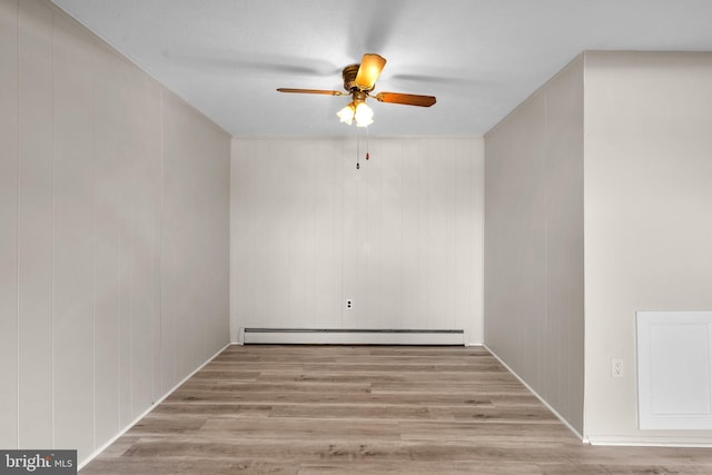 empty room with ceiling fan, wooden walls, baseboard heating, and light hardwood / wood-style flooring