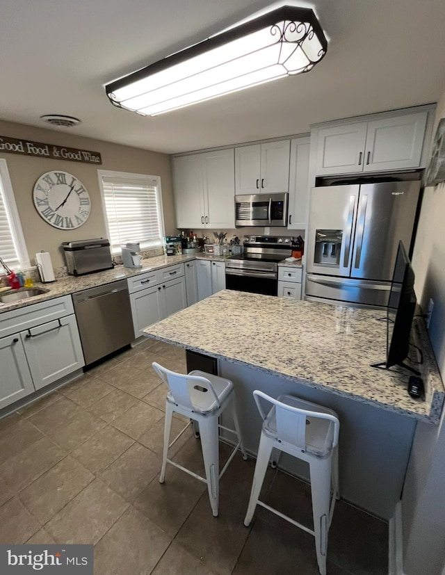 kitchen with sink, a breakfast bar, appliances with stainless steel finishes, white cabinetry, and light stone counters