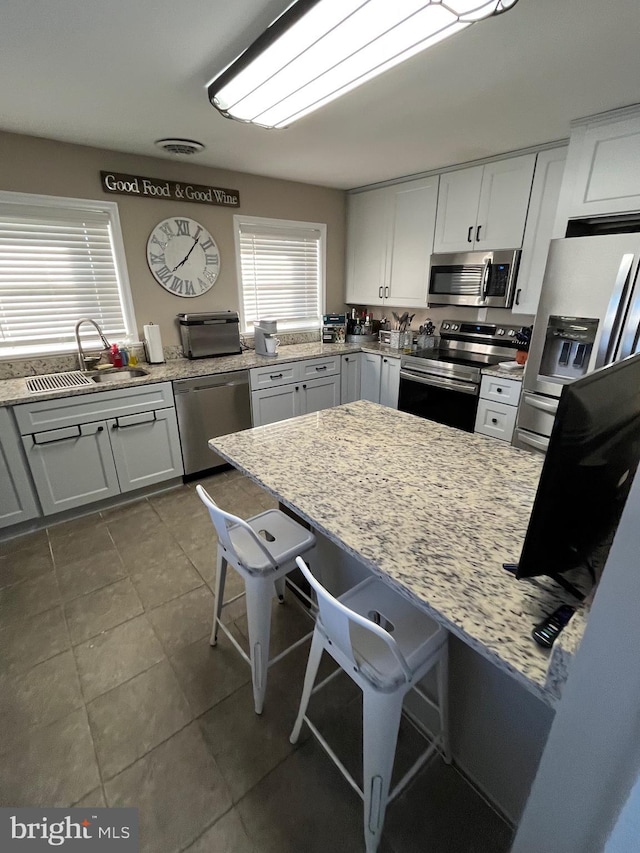 kitchen featuring stainless steel appliances, white cabinetry, light stone countertops, and sink