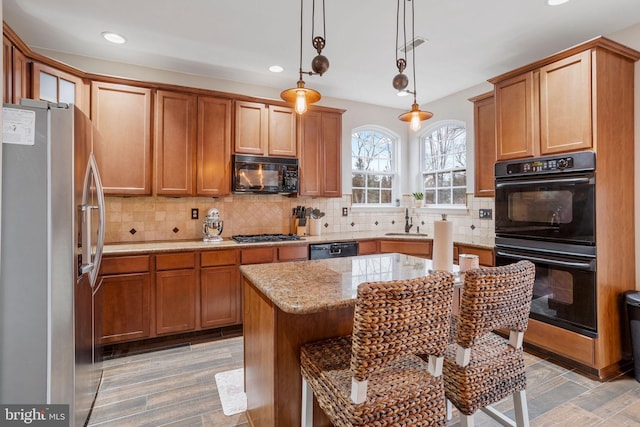 kitchen featuring decorative light fixtures, a kitchen island, black appliances, sink, and light stone countertops