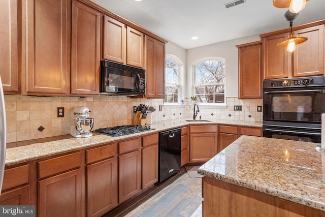 kitchen with light stone counters, sink, decorative light fixtures, and black appliances