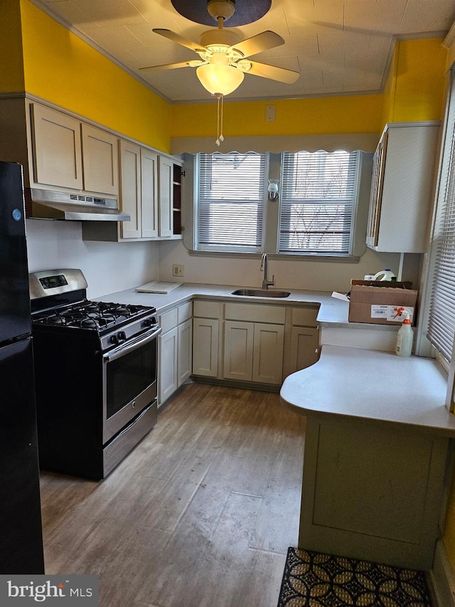 kitchen featuring stainless steel gas range oven, black refrigerator, ceiling fan, sink, and light wood-type flooring