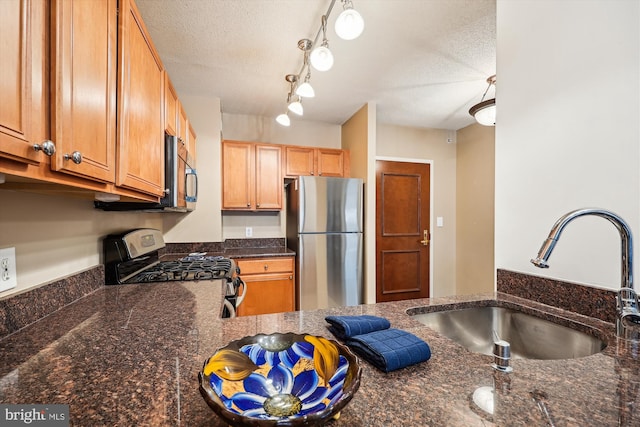 kitchen with sink, a textured ceiling, appliances with stainless steel finishes, and dark stone counters