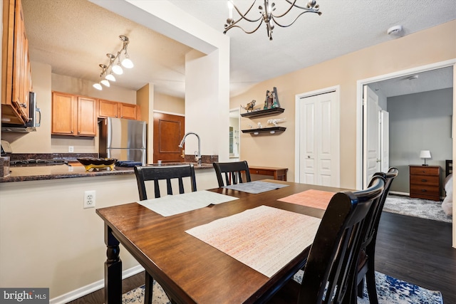 dining room featuring sink, a textured ceiling, dark hardwood / wood-style flooring, and an inviting chandelier