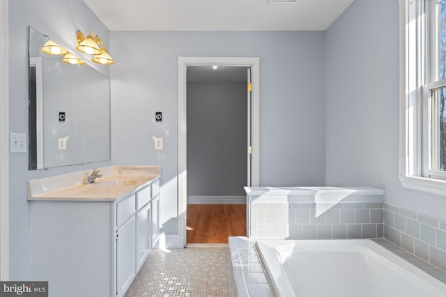 bathroom featuring a relaxing tiled tub and vanity