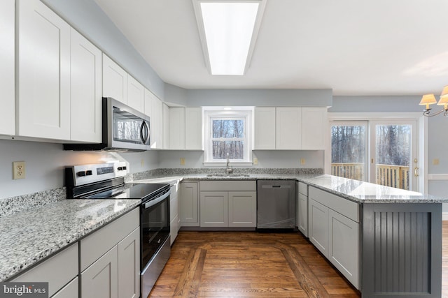 kitchen with stainless steel appliances, sink, light stone counters, and kitchen peninsula