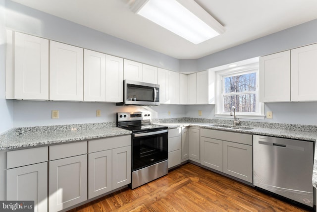 kitchen featuring appliances with stainless steel finishes, sink, white cabinets, light stone countertops, and dark wood-type flooring