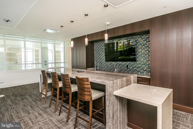 bar with light stone countertops, dark brown cabinets, and pendant lighting