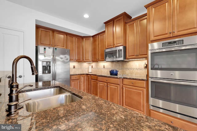 kitchen featuring appliances with stainless steel finishes, sink, backsplash, and dark stone counters