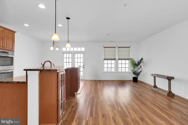 kitchen featuring sink, dark stone counters, hanging light fixtures, dark wood-type flooring, and stainless steel double oven