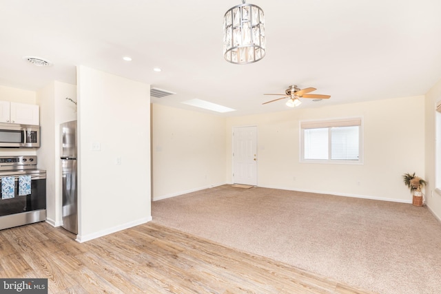 unfurnished living room featuring light carpet and ceiling fan with notable chandelier