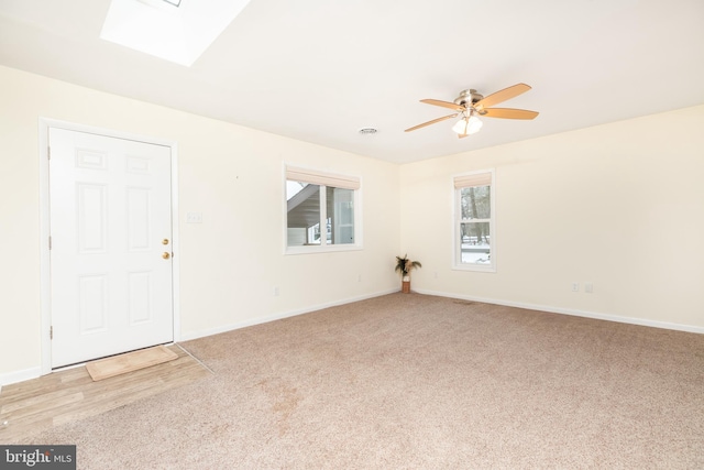 empty room featuring light carpet, a skylight, and ceiling fan