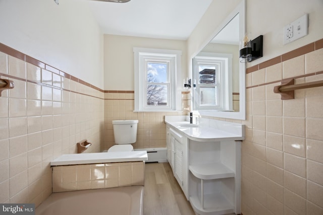 bathroom featuring toilet, vanity, tile walls, wood-type flooring, and a baseboard radiator