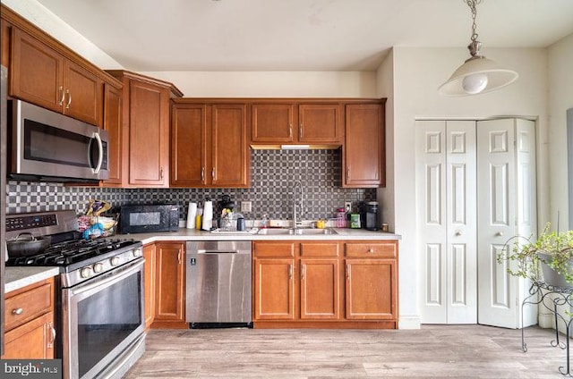 kitchen with sink, tasteful backsplash, hanging light fixtures, light wood-type flooring, and appliances with stainless steel finishes