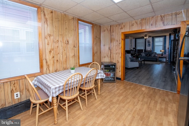 dining area with ceiling fan, a paneled ceiling, wooden walls, and light hardwood / wood-style floors