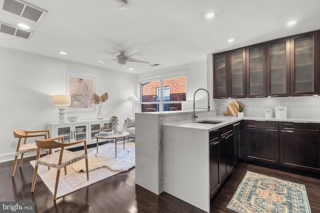 kitchen featuring kitchen peninsula, decorative backsplash, sink, dark brown cabinetry, and dark wood-type flooring