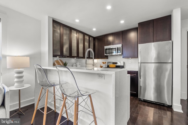 kitchen with tasteful backsplash, a breakfast bar, dark brown cabinetry, appliances with stainless steel finishes, and dark hardwood / wood-style flooring