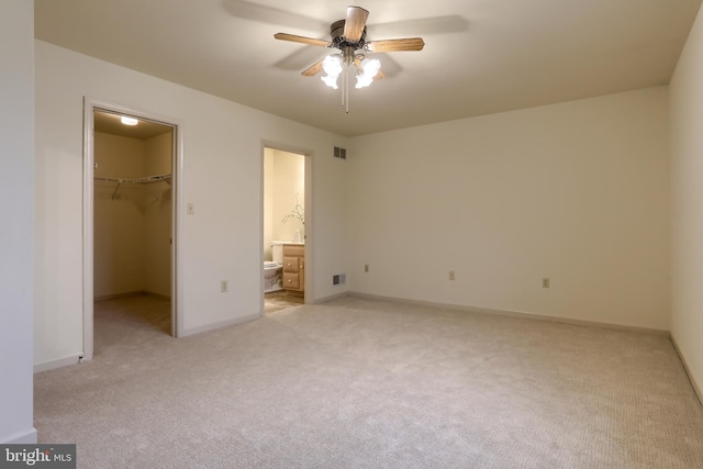 unfurnished bedroom featuring ceiling fan, connected bathroom, light carpet, a walk in closet, and a closet