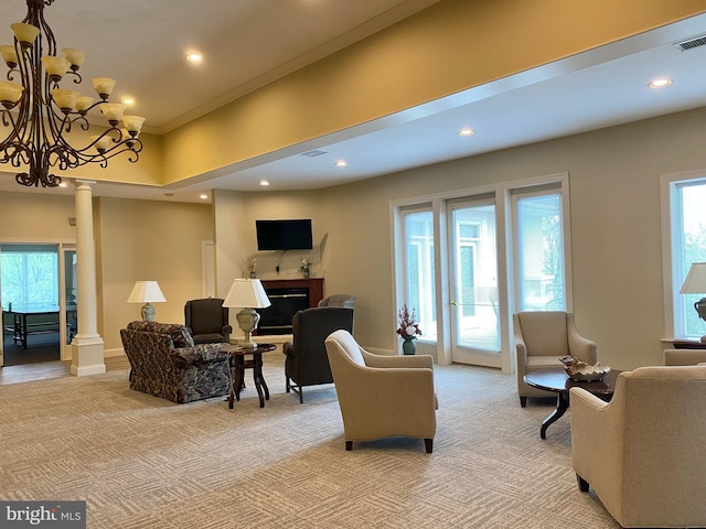 carpeted living room with a notable chandelier, ornamental molding, and decorative columns