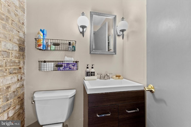 bathroom featuring toilet, vanity, and brick wall