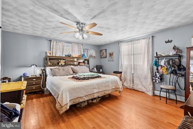 bedroom with a baseboard heating unit, ceiling fan, a textured ceiling, and hardwood / wood-style floors