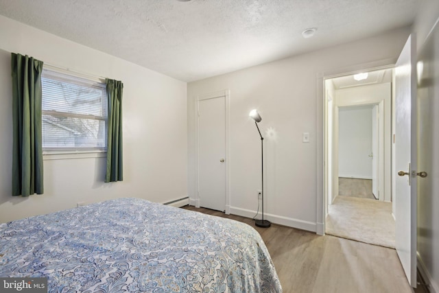 bedroom with light hardwood / wood-style floors, baseboard heating, and a textured ceiling