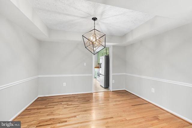 unfurnished dining area featuring an inviting chandelier, a textured ceiling, and light wood-type flooring