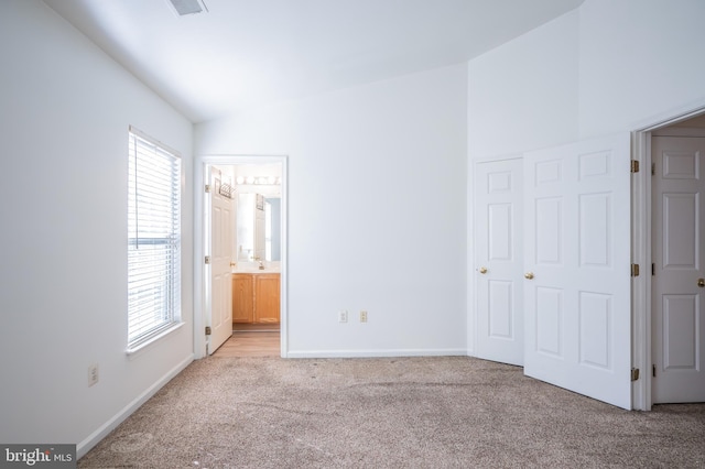 unfurnished bedroom featuring lofted ceiling, light carpet, and connected bathroom