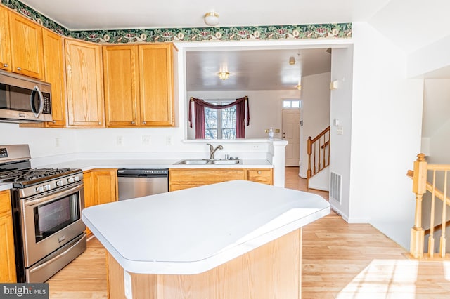 kitchen with stainless steel appliances, a kitchen island, sink, and light hardwood / wood-style floors