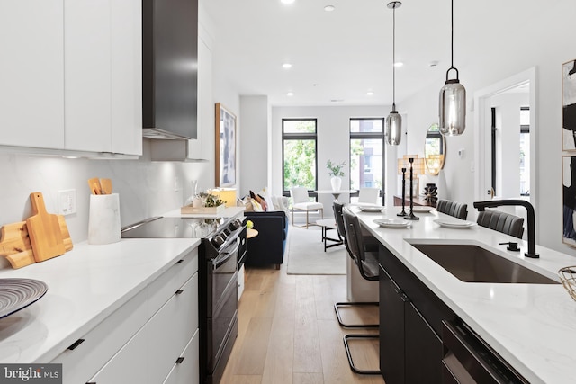 kitchen featuring a breakfast bar area, black electric range oven, white cabinets, and decorative light fixtures