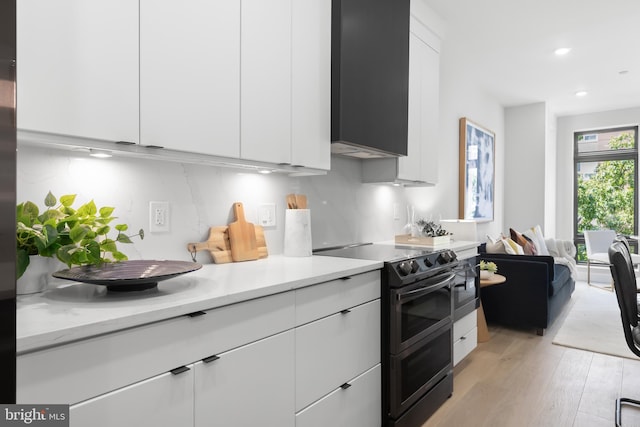 kitchen featuring white cabinetry, range with two ovens, light hardwood / wood-style floors, decorative backsplash, and light stone counters