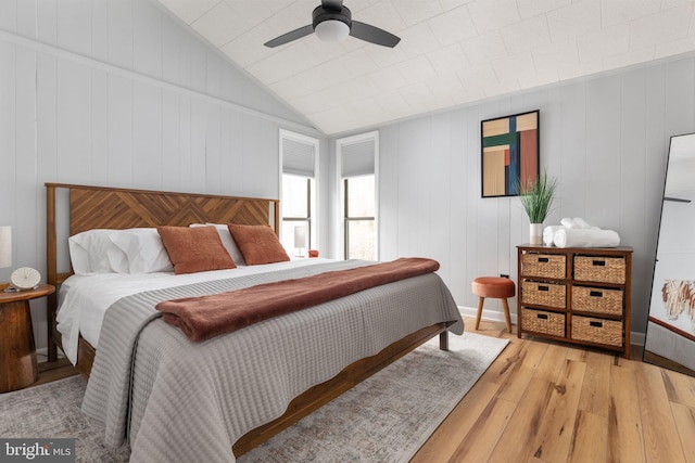 bedroom featuring ceiling fan, light hardwood / wood-style floors, and wood walls