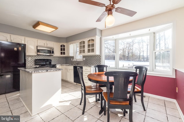 kitchen with backsplash, light tile patterned floors, black appliances, and light stone countertops