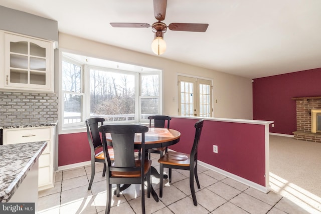 dining area featuring light tile patterned flooring, ceiling fan, a fireplace, and french doors