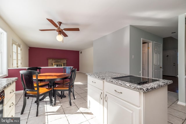 kitchen with light stone counters, white cabinetry, a brick fireplace, a kitchen island, and black electric stovetop