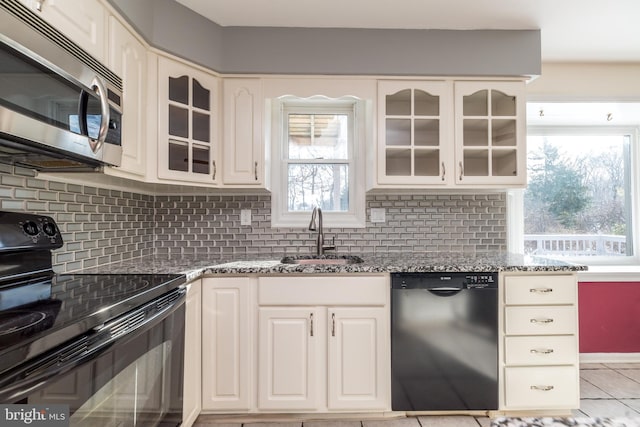 kitchen featuring sink, decorative backsplash, dark stone counters, light tile patterned floors, and black appliances