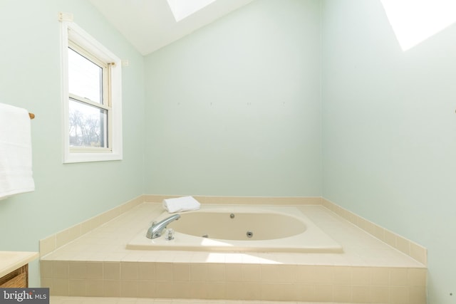 bathroom with a relaxing tiled tub, vanity, and vaulted ceiling with skylight